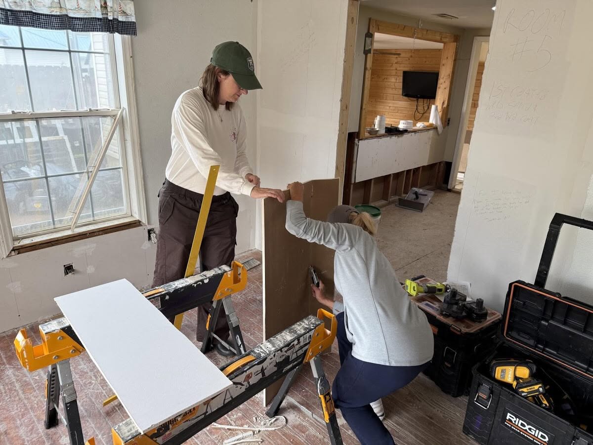 Two volunteers hanging drywall inside a flood-damaged home