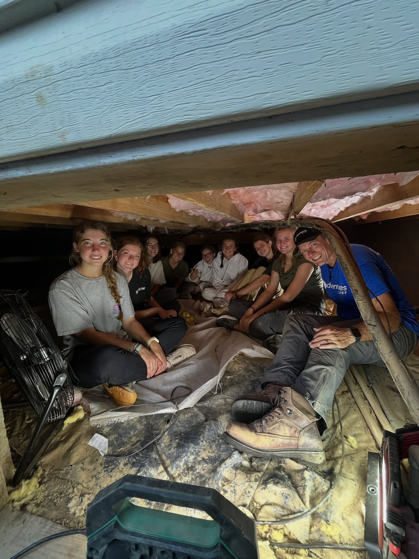 Volunteer crew smiling together in a crawlspace during a repair